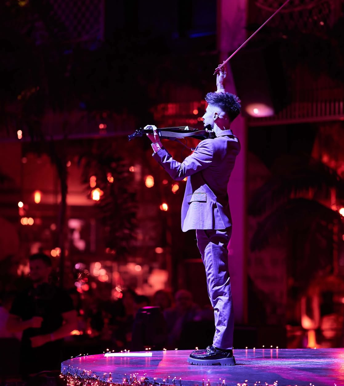 Máté Kozma on stage with bow raised in dramatic red and purple lighting