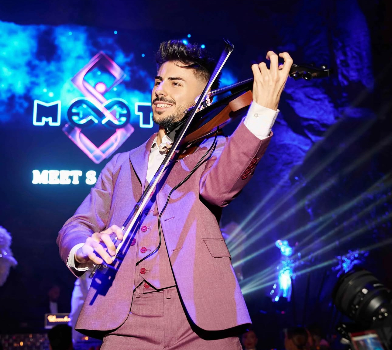 Máté Kozma performing electric violin in purple suit under stage lights